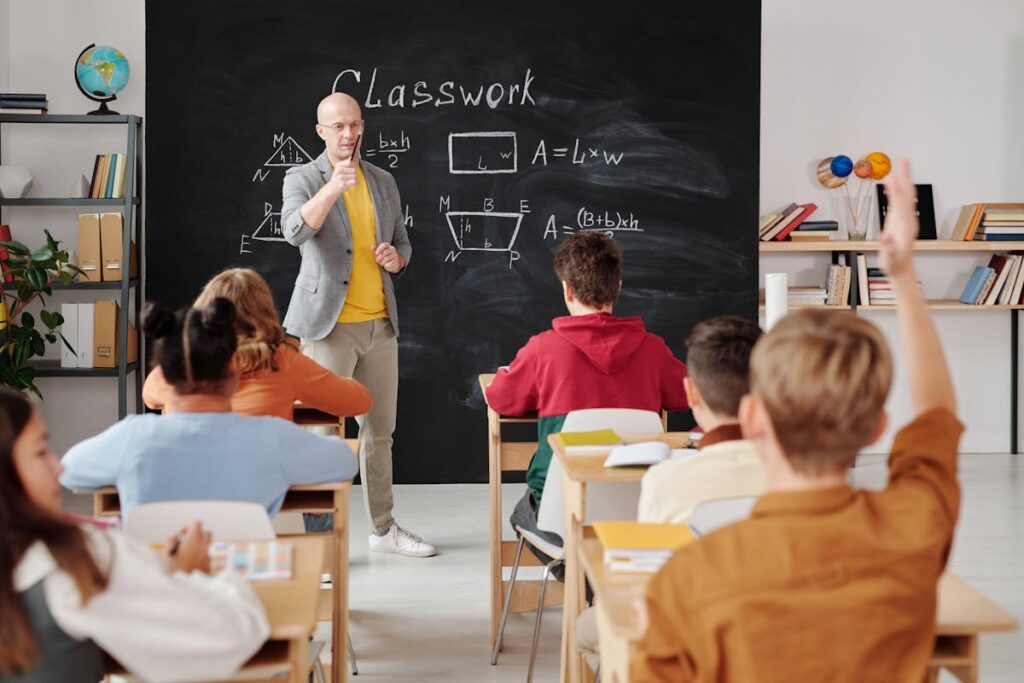 A student raising his hand in a classroom while the teacher points at him